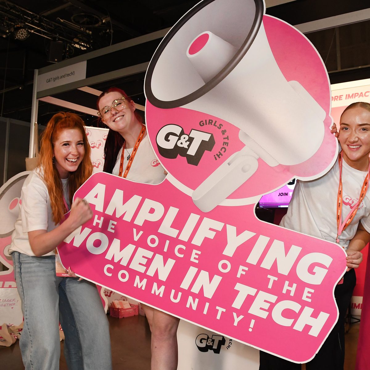 A stand team holding a giant pink megaphone sign about amplifying women in tech
